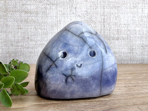 small cloud raku ceramic sculpture glazed in a bottom-to-top gradient of violet to blue to pale blue, almost white at the top. it has an adorable, happy face and is shaped vaguely like a squat raindrop.