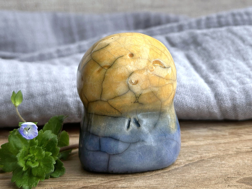 a smiley and loving Jizo Shinto raku ceramic sculpture talisman glazed in a bottom-to-top gradient of blue to golden yellow. they have a kind, gentle face and are a wonderful smooth shape to hold in the hand.