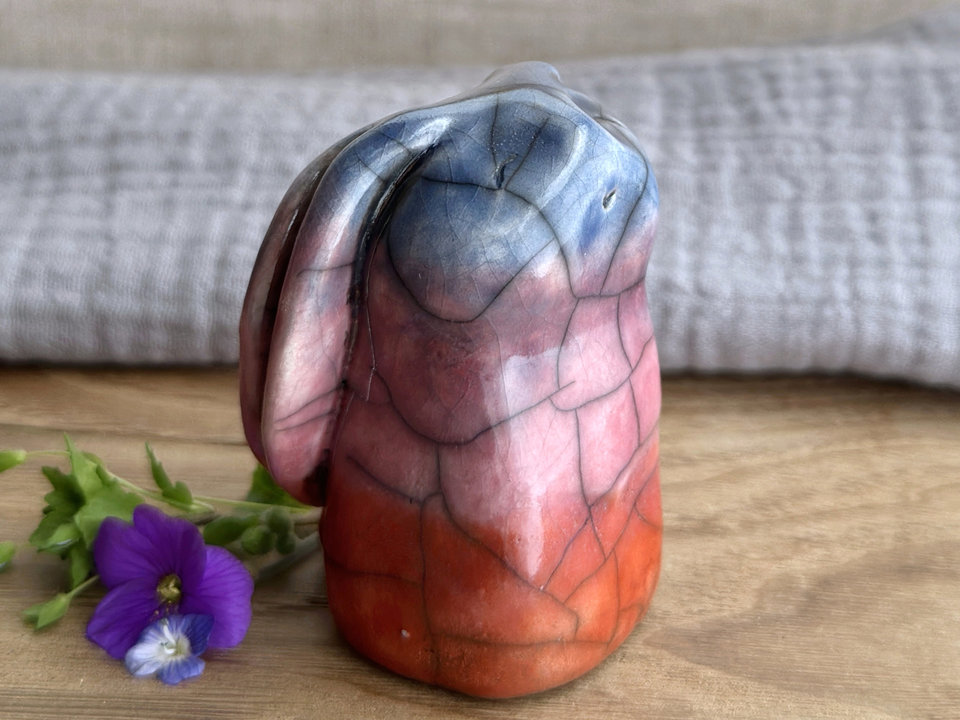Raku ceramic usagi rabbit kami nature spirit glazed in a bottom-to-top gradient of burnt orange to mauve to blue-violet. Its ears are folded down its back, and it has a kind, gentle face.