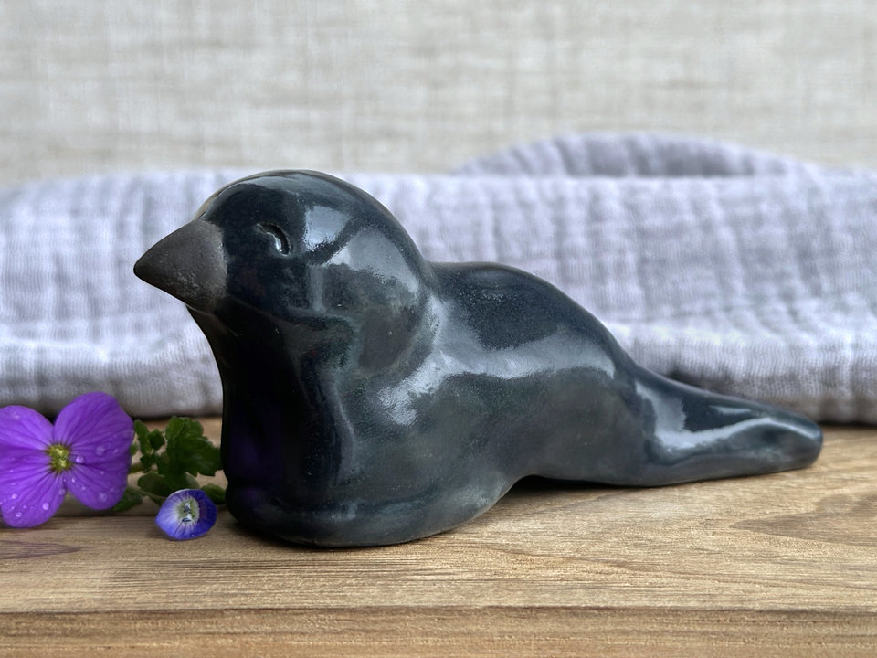 Raku ceramic sculpture of a sitting raven. It is glazed in dark blue-grey, and its beak is left natural, unglazed black.