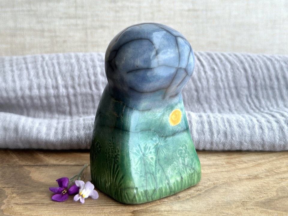 Raku ceramic earth spirit sculpture glazed in spring green, forest green, and blue (bottom to top). She has plant shapes and flowers carved into her and a yellow sun carving too.