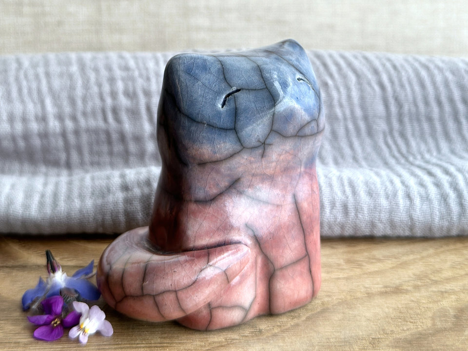 A calm and gentle Shinto Inari nighttime kitsune fox spirit ceramic raku statue glazed in a bottom-to-top gradient of soft pink-orange-red to mauve to blue. Its tail is curled around the right side of its body, and it has a kind face.