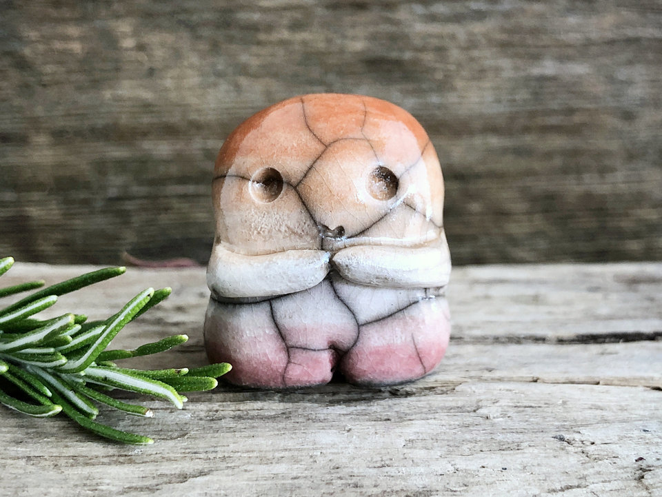 A sweet little nature spirit ceramic guardian statue glazed in the lesbian flag orange, white, and pink colours and with a lovely, gentle face and little arms. It has a small branch design carved up one side.