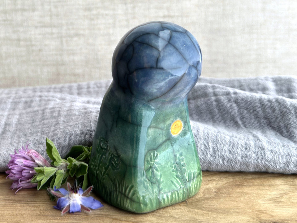 Raku ceramic earth spirit sculpture glazed in spring green, forest green, and blue (bottom to top). She has plant shapes and flowers carved into her and a yellow sun carving too.