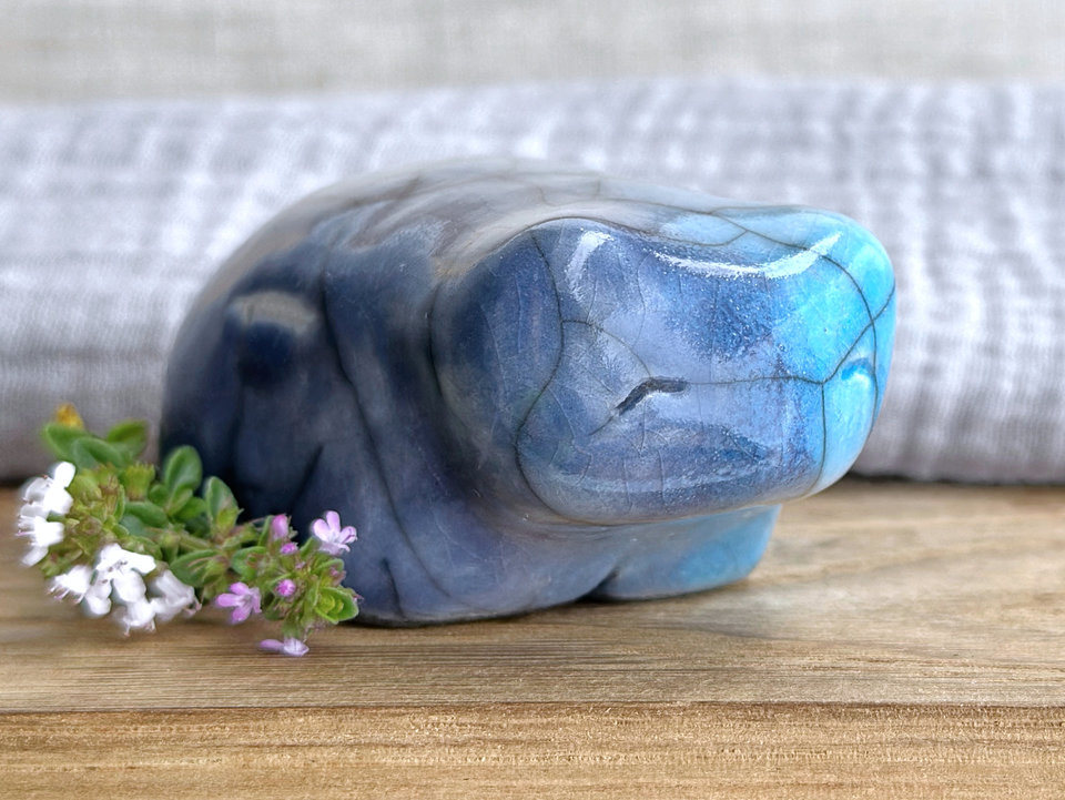 Ceramic raku bear kami sculpture glazed in turquoise mostly on its right side and blue mostly on its left side. It has a kind, gentle face and is a little chonky. It also has a white, scar-like mark on its left side.