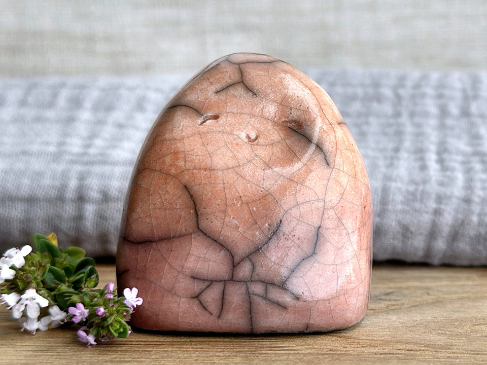 vaguely dome-shaped nature spirit ceramic sculpture. it is glazed in a bottom-to-top gradient of a soft bordeaux red to soft peach. it has a gentle, smiling face.