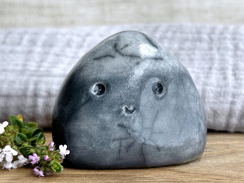 small cloud raku ceramic sculpture glazed in a bottom-to-top gradient of grey to almost white at the top. it has a happy face and is shaped vaguely like a squat raindrop.