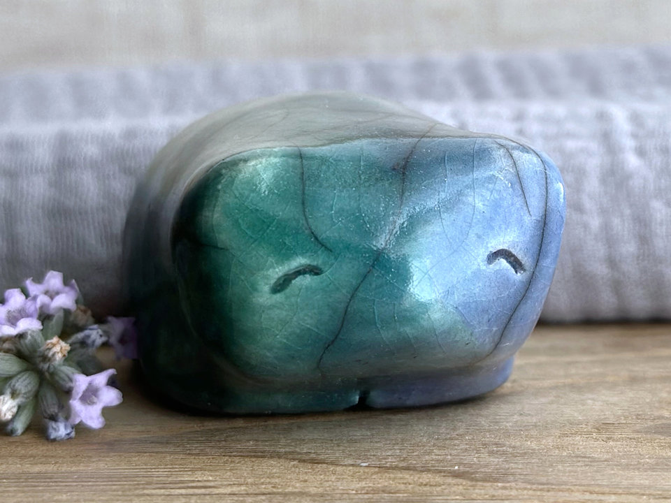 Raku ceramic bear kami sculpture glazed in forest green mostly on its left side and blue mostly on its right side. Where they overlap is a beautiful aqua colour. It has a kind, gentle face and is a little chonky.