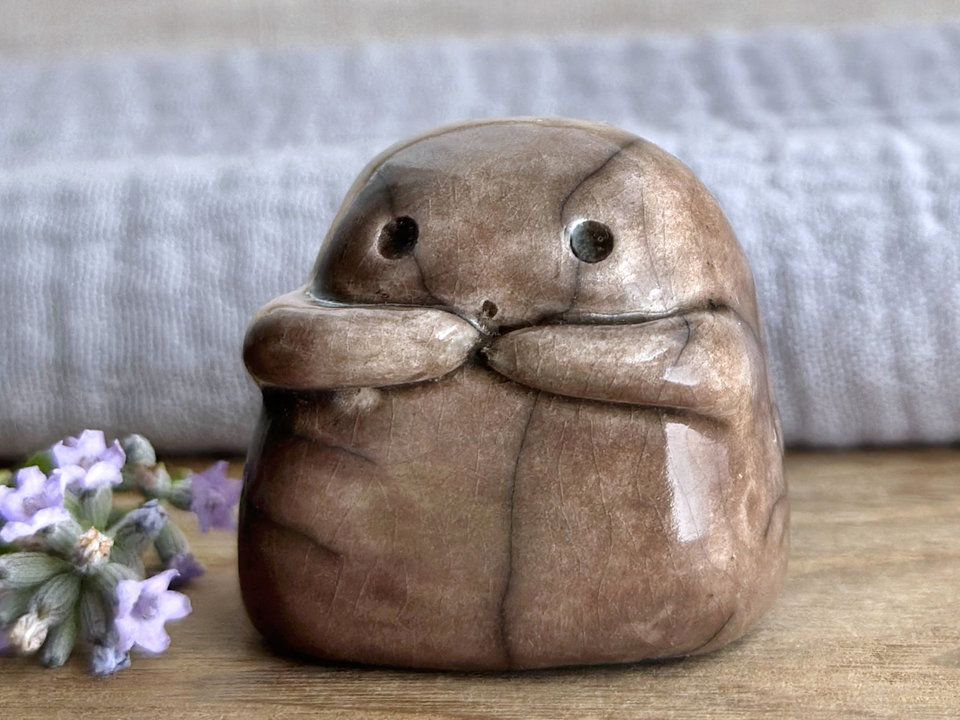 A sweet little kodama nature spirit ceramic guardian statue glazed in brown and with a lovely, gentle face and little arms.