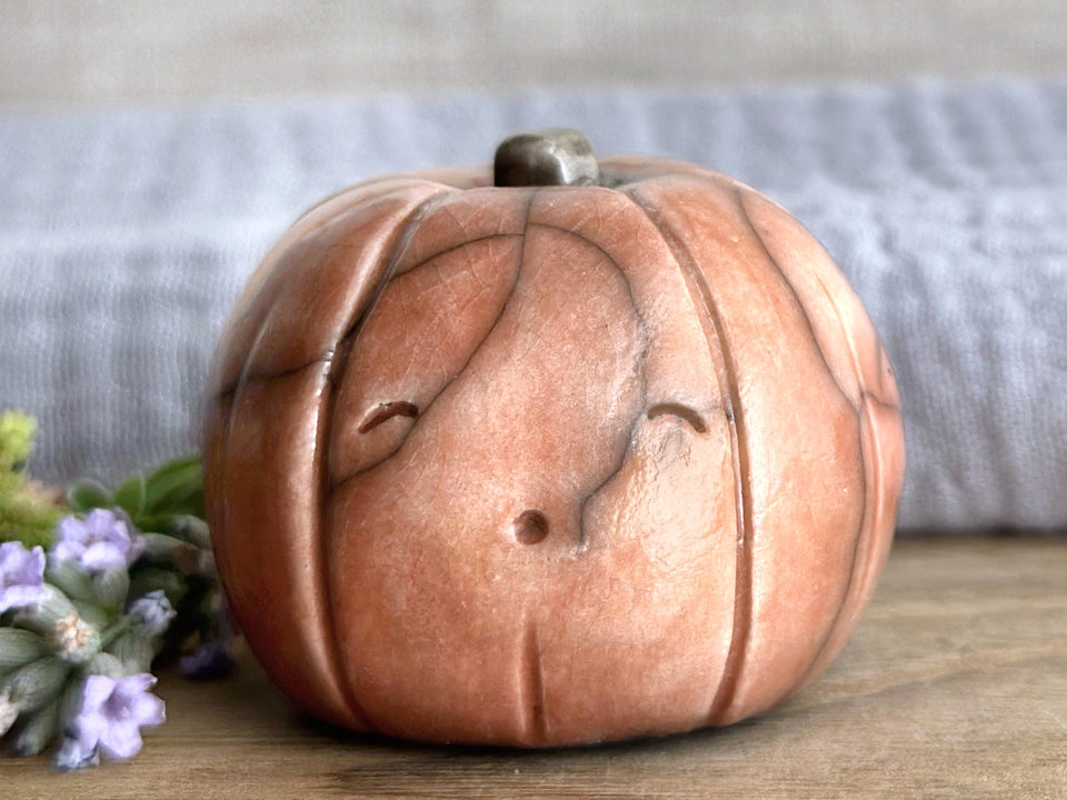 raku ceramic orange pumpkin nature spirit sculpture with a smiling eyes and an oooo mouth. it has a cute little green-brown stalk on top.