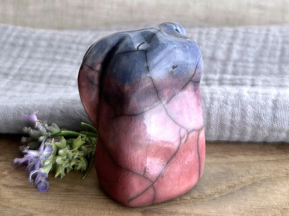 Raku ceramic usagi rabbit kami nature spirit glazed in a bottom-to-top gradient of warm soft red-pink to mauve to blue. Its ears are folded down its back, and it has a kind, gentle, smiling face.