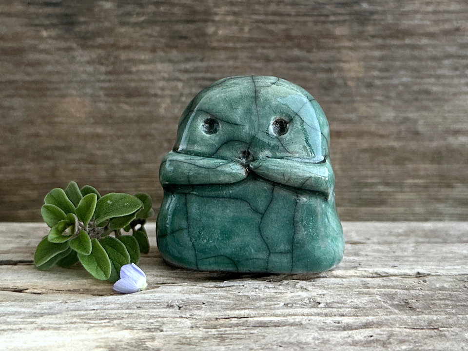 A sweet little kodama nature spirit ceramic guardian statue glazed in forest green and with a lovely, gentle face and little arms.