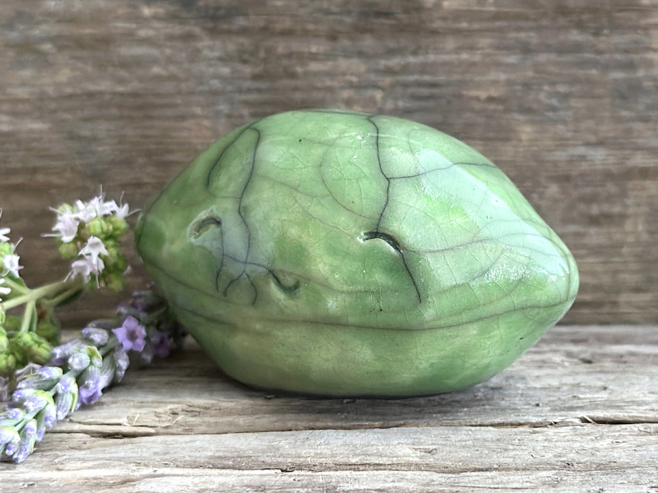 a very happy raku ceramic sculpture of a lime or a lemon. it's glazed in a soft bright green colour.