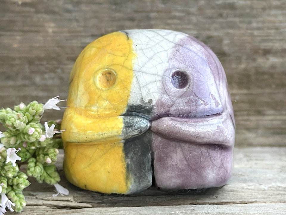 a sweet little nature spirit ceramic guardian statue glazed in the nonbinary flag black, purple, white and yellow colours and with a lovely, gentle face and little arms. It has a small branch design carved up one side.