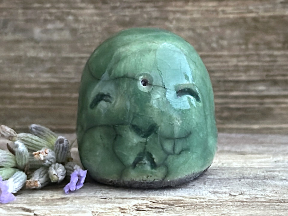 tiny pocket jizo raku sculpture glazed in green. he has a smiling, gentle face.