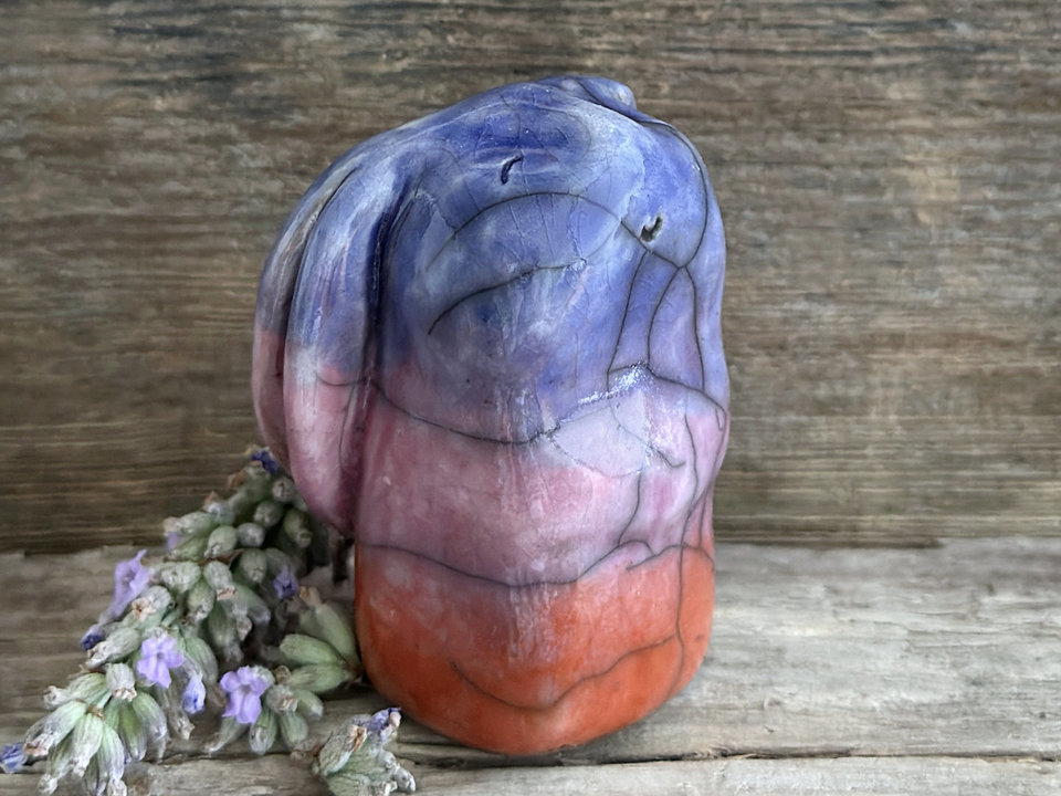 Raku ceramic usagi rabbit kami nature spirit glazed in a bottom-to-top gradient of burnt orange to mauve to indigo-violet. Its ears are folded down its back, and it has a kind, gentle face.