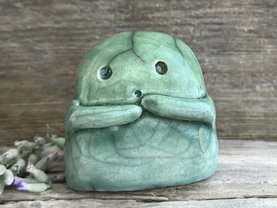 A sweet little kodama nature spirit ceramic guardian statue glazed in shades of green and with a lovely, gentle face and little arms.