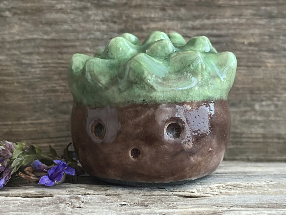 a roundish raku scuplture glazed in warm brown with green for the chestnut spikes on the top of its head. (they're not sharp at all!). it has a cute, open, friendly face.