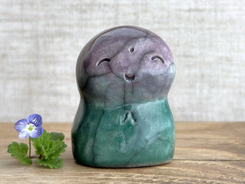 a smiley and loving Jizo Shinto raku ceramic sculpture talisman glazed in a bottom-to-top gradient of forest green to purple. they have a kind, gentle face and are a wonderful smooth shape to hold in the hand.