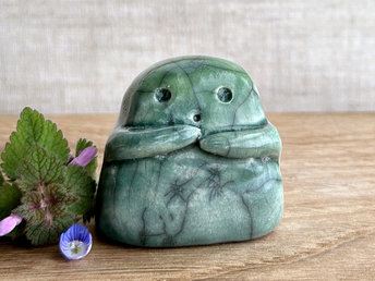 A sweet little kodama nature spirit ceramic guardian statue glazed in shades of green and with a lovely, gentle face and little arms. There are tiny dark grey spiderweb patterns in the glaze, in addition to the normal raku crackles, from where raindrops fell on it.