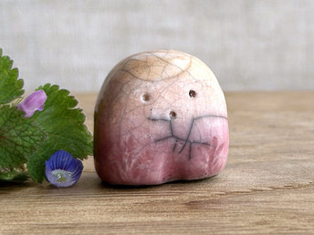 a small and stout nature spirit raku sculpture glazed in peach. it has a cute little face, and little plant carvings on its front. there are tiny dark grey spiderweb patterns in the glaze, in addition to the normal raku crackles, from where raindrops fell on it.