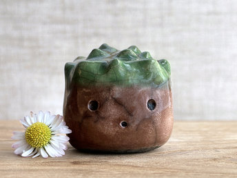 a roundish raku scuplture glazed in warm brown with green for the chestnut spikes on the top of its head. (they're not sharp at all!). it has a cute, open, friendly face.