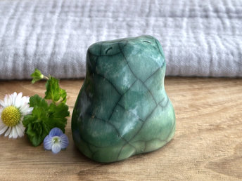 a happy frog raku ceramic sculpture glazed in green at the bottom and forest green everywhere else. it has a kind, happy face and is a lovely shape to hold in the hand.