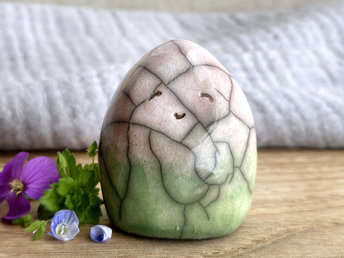 vaguely dome-shaped nature spirit ceramic sculpture. it is glazed in a bottom-to-top gradient of spring green to pale red-pink and has plant and flower carvings on its body. it also has a gentle, smiling face.