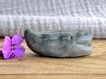 a small, blue-grey whale sculpture. its small tail is raised up, and it has a gently smiley sort of face.