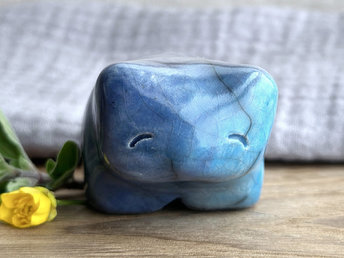 Ceramic raku bear kami sculpture glazed in turquoise mostly on its right side and blue mostly on its left side. It has a kind, gentle face and is a little chonky.