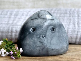 small cloud raku ceramic sculpture glazed in a bottom-to-top gradient of grey to almost white at the top. it has a happy face and is shaped vaguely like a squat raindrop.