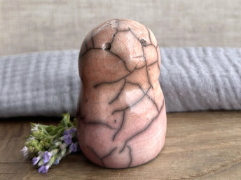 tall raku ceramic bird sculpture glazed in a top-to-bottom gradient of pale peach to pale pinky red. it has a kind, gentle, and slightly concerned face and feels very reassuring to hold. it has some very small, dimpled, pinhole glaze disturbance marks on its body.
