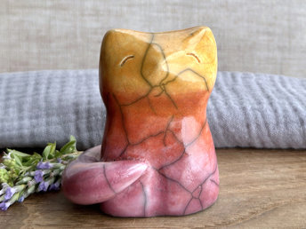 Raku ceramic sitting fox glazed in a gradient from mauve to orange to golden yellow (bottom to top). It has a kind face, and its tail is curled around its body on its right side.