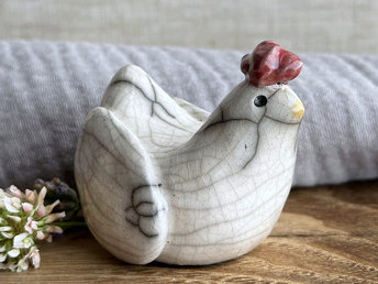 a white raku ceramic chicken with grey eyes, a pale orange beak, and a bordeaux red comb on the top of her head. she looks very sweet.