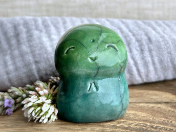 a smiley and loving Jizo Shinto raku ceramic sculpture talisman glazed in a bottom-to-top gradient of forest green to leaf green. they have a kind, gentle face and are a wonderful smooth shape to hold in the hand.