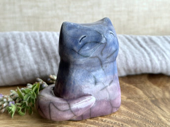 A calm and gentle Shinto Inari nighttime kitsune fox spirit ceramic raku statue glazed in a bottom-to-top gradient of purple to blue. Its tail is curled around the right side of its body, and it has a kind face.