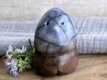 a vaguely dome-shaped nature spirit ceramic sculpture with a gently pointed head and four stubby little legs. it is glazed in a bottom-to-top gradient of brown to blue and has a gentle face with two round eyes and a stubby nose.