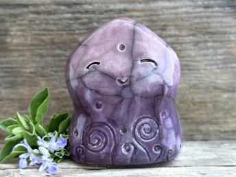a nature spirit sculpture shaped a bit like a wide hourglass that's a little pointy at the top. it is glazed in a bottom-to-top gradient of violet-purple to soft mauve and has spiral carvings on its body. it also has a gentle, happy face.