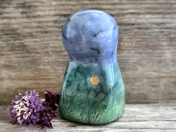 Raku ceramic mother earth spirit spirit sculpture glazed in spring green, forest green, and blue (bottom to top). It has plant shapes and flowers carved into it and a yellow sun carving too.