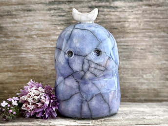 A kodama nature and forest spirit kami ceramic raku sculpture glazed in blue with faint hints of mauve. It has a gentle face, and a white crescent moon on its head.