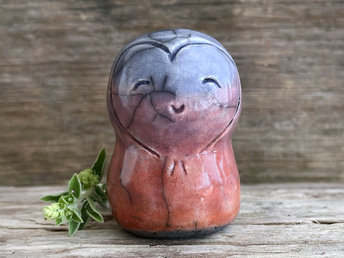 a smiley and loving Jizo Shinto raku ceramic sculpture talisman glazed in a bottom-to-top gradient of soft red-orange to purple to blue. she has a heart shape around her kind, gentle face and is a wonderful smooth shape to hold in the hand.