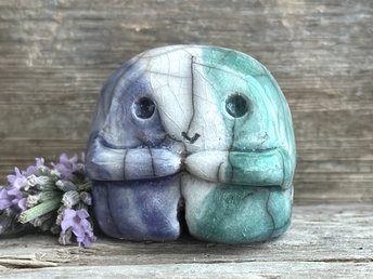 A sweet little nature spirit ceramic guardian statue glazed in the men's gay flag green, white, and blue colours and with a lovely, gentle face and little arms. It has a small branch design carved up one side.