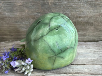 vaguely egg-shaped but quite round and stout nature spirit sculpture. it is glazed in a bottom-to-top gradient of yellow-green to spring green and looks a little like a frog. it has a gentle, happy face.