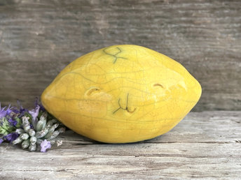 a very happy raku ceramic sculpture of a lemon. it's glazed in a golden yellow colour.