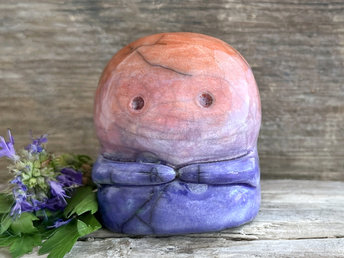 A kodama nature spirit ceramic guardian statue glazed in a bottom-to-top gradient of indigo to violet to mauve to red-orange. It has a wide face, two big eyes, and cute little arms.