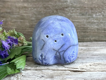 a small and stout nature spirit raku sculpture glazed in blue. it has a cute little face, and flower and plant carvings on its front.