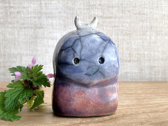 A kodama nature and forest spirit kodama kami ceramic raku sculpture glazed in a bottom-to-top gradient of red-orange to mauve to purple to indigo. It has a gentle face, and a white crescent moon on its head.